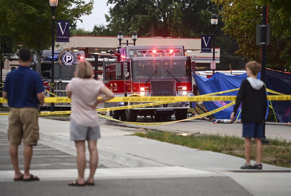 Onlookers gather from across the street to see law enforcement and firefighters work the scene of a plane crash, Sunday, Aug. 8, 2021 in Victoria, Minn. Three people died when a single-engine plane crashed into a vacant lot and burst into flames in a small southeastern Minnesota city, a National Transportation Safety Board official said Sunday.(Aaron Lavinsky/Star Tribune via AP)