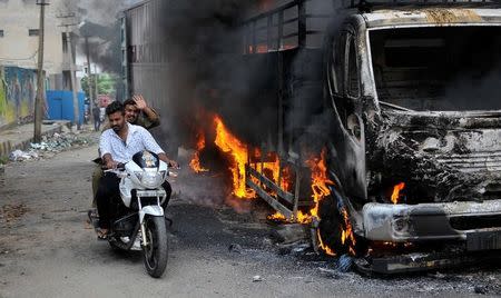 Men ride a motorcycle past a lorry in Bengaluru, which was set on fire by protesters after Supreme Court ordered Karnataka to release 12,000 cubic feet of water per second every day from the Cauvery river to neighbouring Tamil Nadu, India September 12, 2016. REUTERS/Abhishek N. Chinnappa