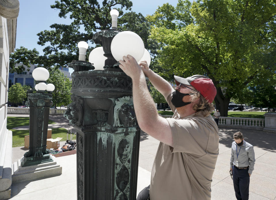 Jeremy Thompson with DOA replaces broke lights at the West Washington entrance to the state Capitol in Madison, Wis., the morning after protesters tore down statues of Forward and a Union Civil War colonel. Protesters also assaulted a state senator and damaged the Capitol Tuesday night after the arrest of a Black activist earlier in the day. (Steve Apps/Wisconsin State Journal via AP)