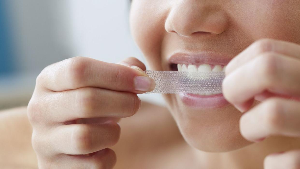 close up of young woman using a teeth whitening strip