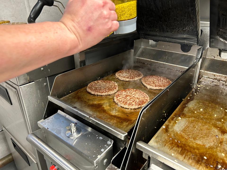 Cooked burger patties on a grill, with seasoning being added.