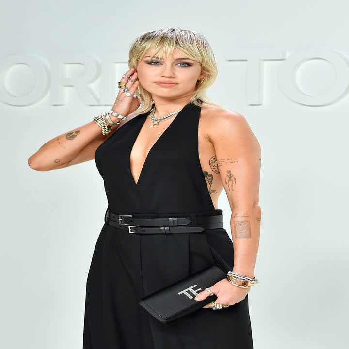 Miley Cyrus poses on the red carpet at an event in a halter belted dress