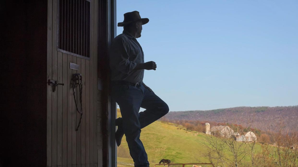 "Farmer silhouette in open barn door with farm scenery in background, having a smoke in a leaning relaxation pose, a farm in Pennsylvania, PA, USA.