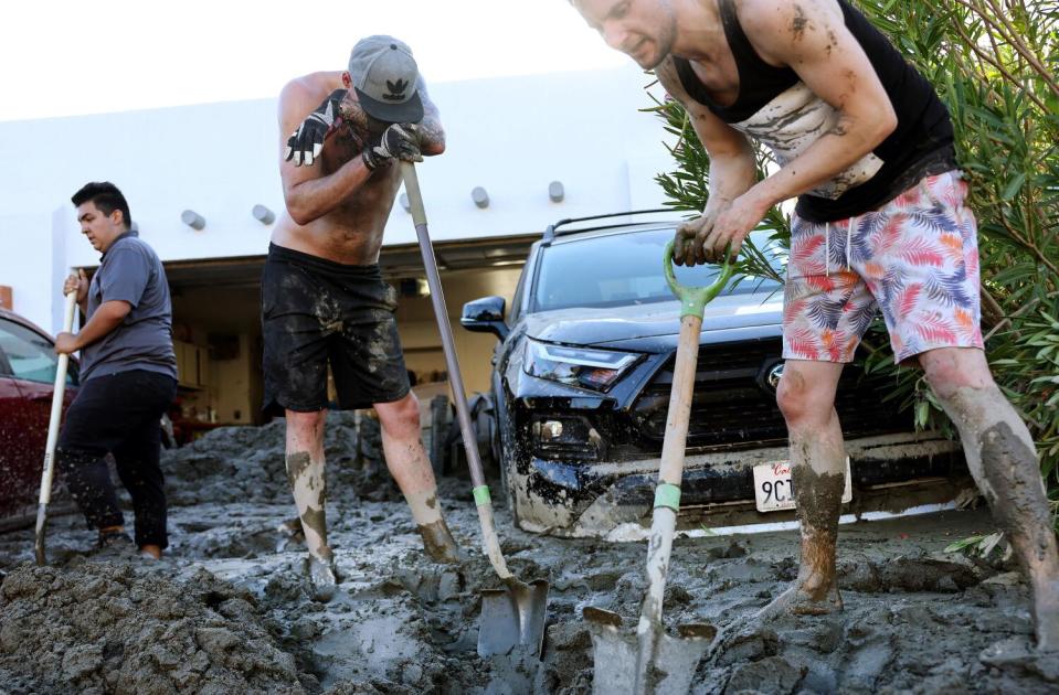 Men shovel deep mud from a residential driveway.