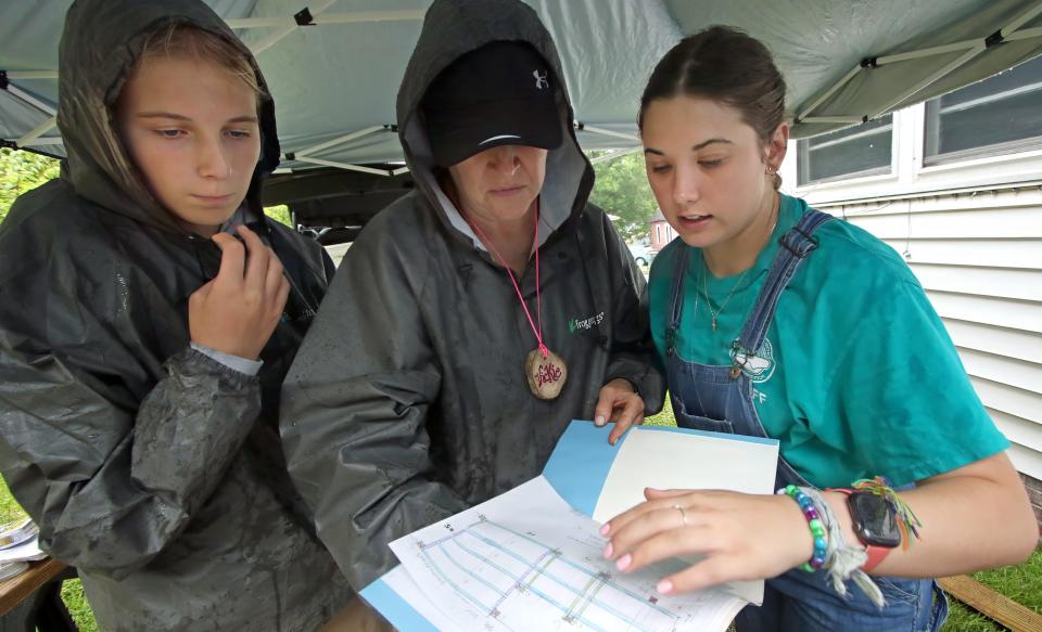 Ansley Robinson, Vickie Robinson and Bree Eldridge stay dry as they look over construction plans as a group from Carolina Cross Connections  construct a ramp at a home on South Marietta Street in the rain Thursday morning, June 22, 2023.