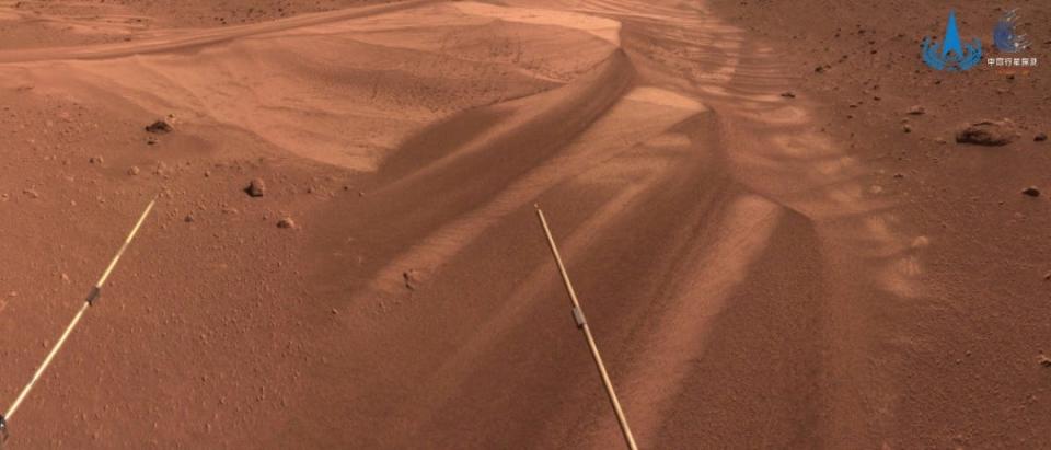 ridges of brown red sand on mars with two rover antennae in the foreground