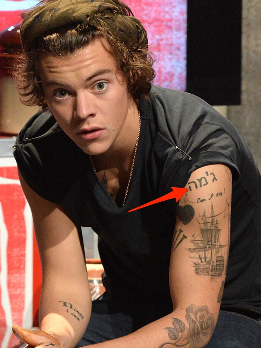 A red arrow pointing to a tattoo written in Hebrew on Harry Styles' bicep.