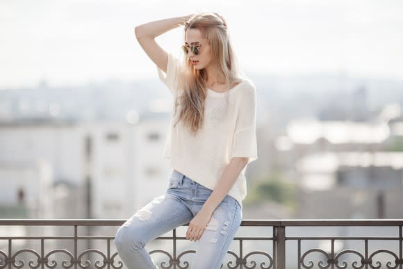 Female fashion model perched on a railing outdoors, with a city in the background