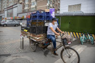 A man wearing a face mask to protect against the coronavirus pedals a cycle loaded with boxes and crates in Beijing, Saturday, July 11, 2020. New coronavirus cases have dropped sharply in China, and authorities are turning their attention to concerns that the virus could spread through imported food. (AP Photo/Mark Schiefelbein)