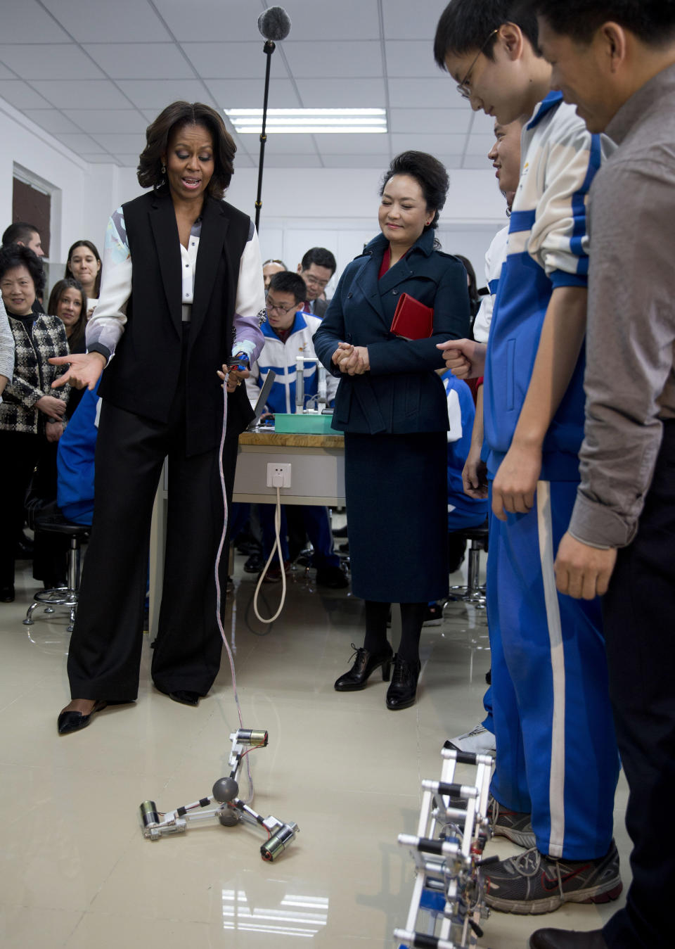 U.S. first lady Michelle Obama, left, tries out a remote control mechanical robot next to Peng Liyuan, wife of Chinese President Xi Jinping as they visit the Beijing Normal School, a school that prepares students to attend university abroad in Beijing, China Friday, March 21, 2014. (AP Photo/Andy Wong, Pool)