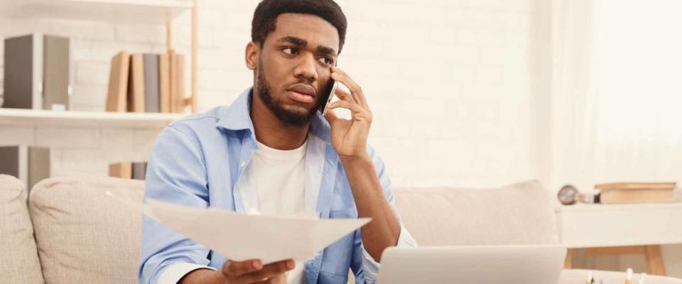 Discussing document. Serious african-american man holding paper and talking on mobile phone, working at home office, copy space