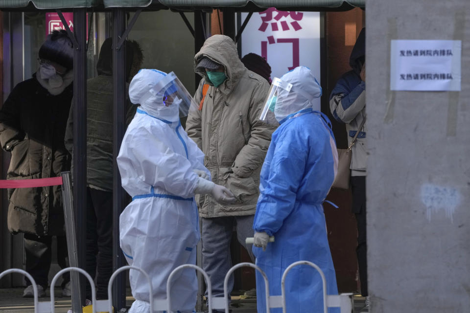 Medical workers in protective gear chat each other as residents wait to enter the fever clinic of a hospital in Beijing, Tuesday, Dec. 13, 2022. Some Chinese universities say they will allow students to finish the semester from home in hopes of reducing the potential of a bigger COVID-19 outbreak during the January Lunar New Year travel rush. (AP Photo/Andy Wong)