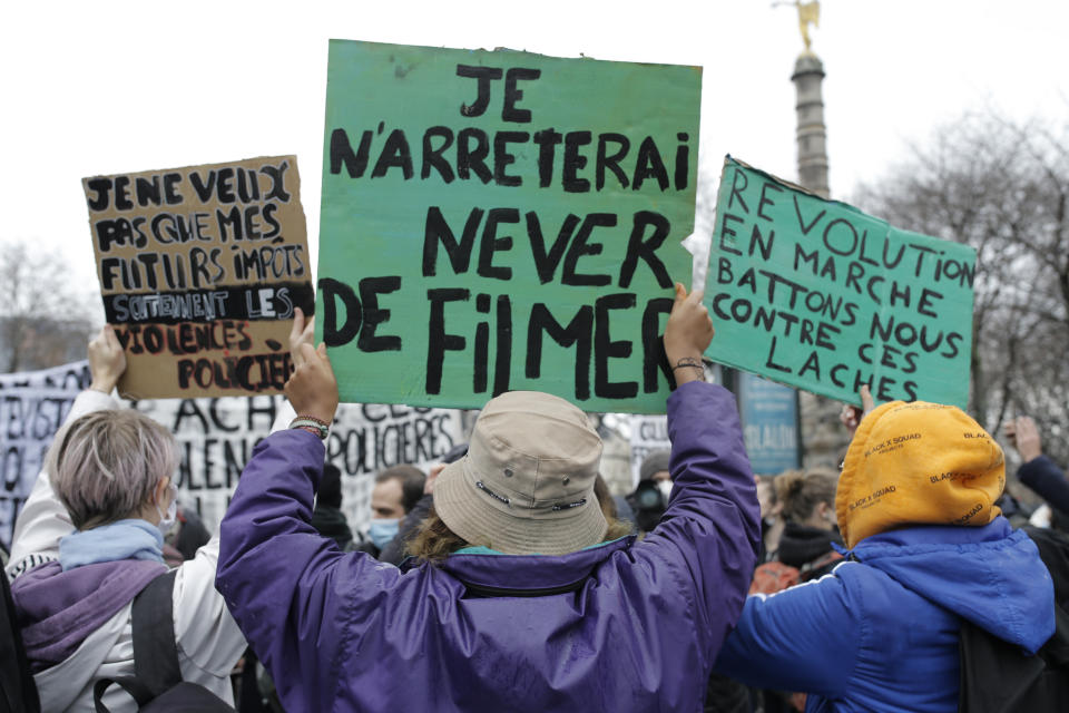 A demonstrator, center, holds a poster "I will never stop filming" during a protest, Saturday, Dec.12, 2020 in Paris. Protests are planned in France against a proposed bill that could make it more difficult for witnesses to film police officers. (AP Photo/Lewis Joly)