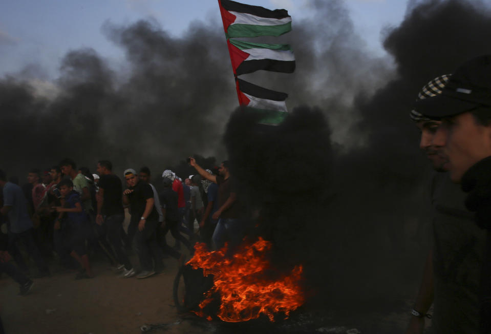 Protesters burn tires while other wave his national near the fence of the Gaza Strip border with Israel east of Khan Younis, southern Gaza Strip, Friday, Oct. 19, 2018. (AP Photo/Adel Hana)