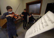 Hildegard De Stefano, left, plays her violin and Denis Malakhof, right, plays the piano during a lesson with maestro Luca Braga, all wearing face masks to curb the spread of COVD-19, at the Giuseppe Verdi Music Conservatory, in Milan, Italy, Thursday, April 29, 2021. Whatever the instrument, flute, violin or drums, students at Italy's oldest and largest music conservatory have been playing behind plexiglass screens during much of the pandemic as the Conservatory found ways to preserve instruction throughout Italy’s many rolling lockdowns. (AP Photo/Antonio Calanni)