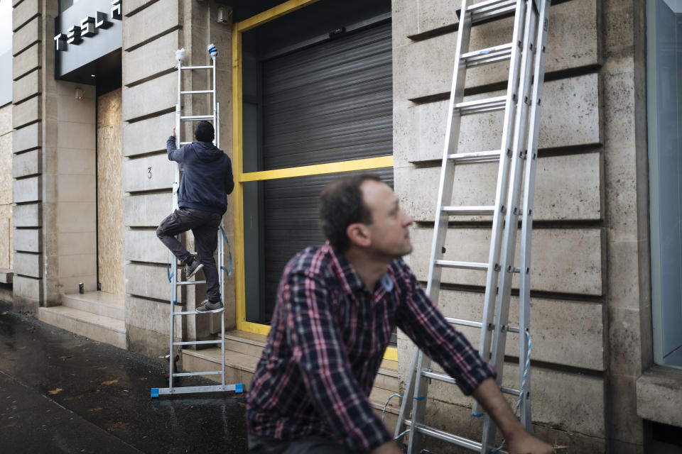 A man climbs on a ladder as he tries to fix the front of his shop near the Madeleine Church in Paris, Sunday, Dec. 2, 2018. A protest against rising taxes and the high cost of living turned into a riot in the French capital Saturday, as activists caused widespread damage and tagged the Arc de Triomphe with multi-colored graffiti during clashes with police. (AP Photo/Kamil Zihnioglu)