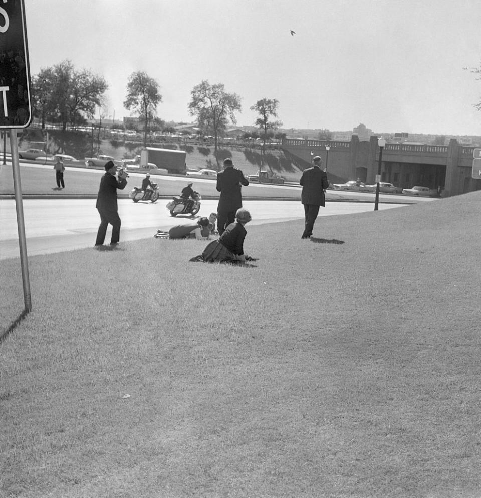 A newsreel cameraman stands at the left as spectators hug the ground moments after a sniper's bullet ended President Kennedy's life