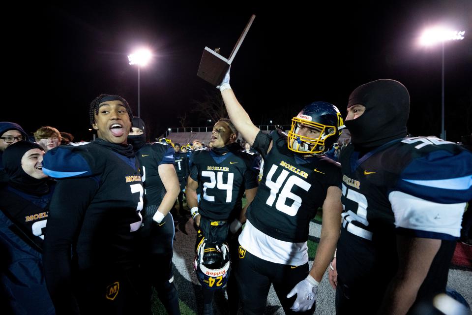 Moeller linebacker Joseph Ginnetti (46) holds up the regional trophy while celebrating with running back Jordan Marshall (24), defensive back Karson Hobbs (3) and offensive lineman Collin Remenowsky (52) after the OHSAA regional final Friday.
