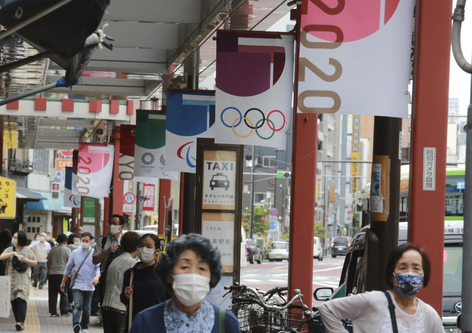 People wearing face masks to help protect against the spread of the coronavirus walk under the banner of Tokyo Olympics along a walkway in Tokyo, Wednesday, June 30, 2021. (AP Photo/Koji Sasahara)