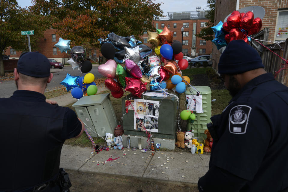 Members of Valentis Private Security pause at a makeshift memorial of balloons, stuffed animals, and photographs, Monday, Nov 6, in Cincinnati, for Dominic Davis, an 11-year-old boy, who was killed in a weekend shooting. Police Chief Terri Theetge told reporters Sunday that a shooter in a sedan fired 22 rounds "in quick succession" into a crowd of children just before 9:30 p.m. Friday on the city's West End. (AP Photo/Carolyn Kaster)