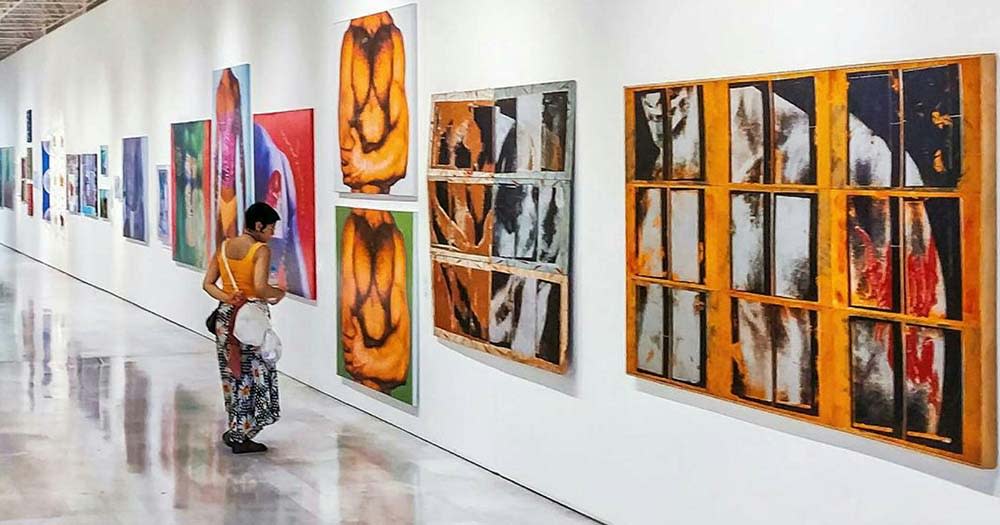 Photo of a person looking at paintings hanging on the wall representing the upcoming LGBT art exhibition