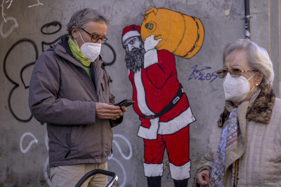 A man and woman wearing FFP2 masks to curb the spread of COVID-19 are seen in front of a mural depicting Santa Claus, in Madrid, Spain, Wednesday, Jan. 12, 2022. Italy, Spain and other European countries are re-instating or stiffening mask mandates as their hospitals struggle with mounting numbers of COVID-19 patients. (AP Photo/Manu Fernandez)