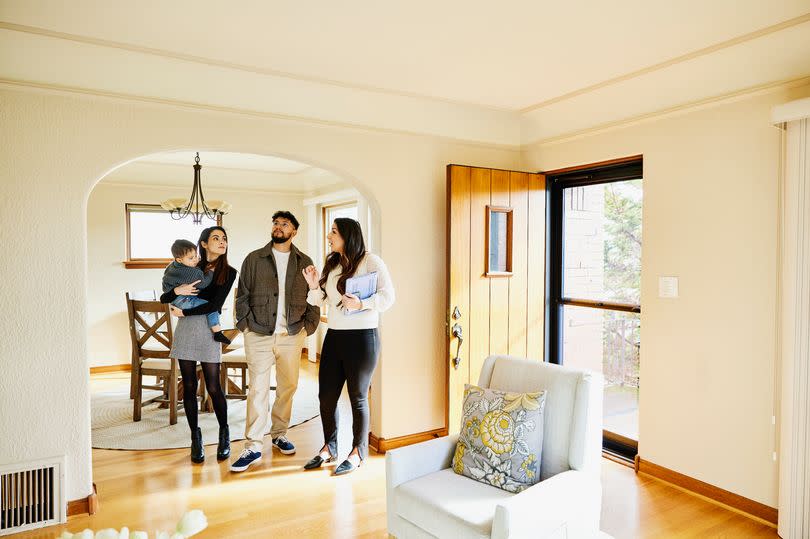 Wide shot for family with toddler in discussion with real estate agent while looking home for sale during open house.