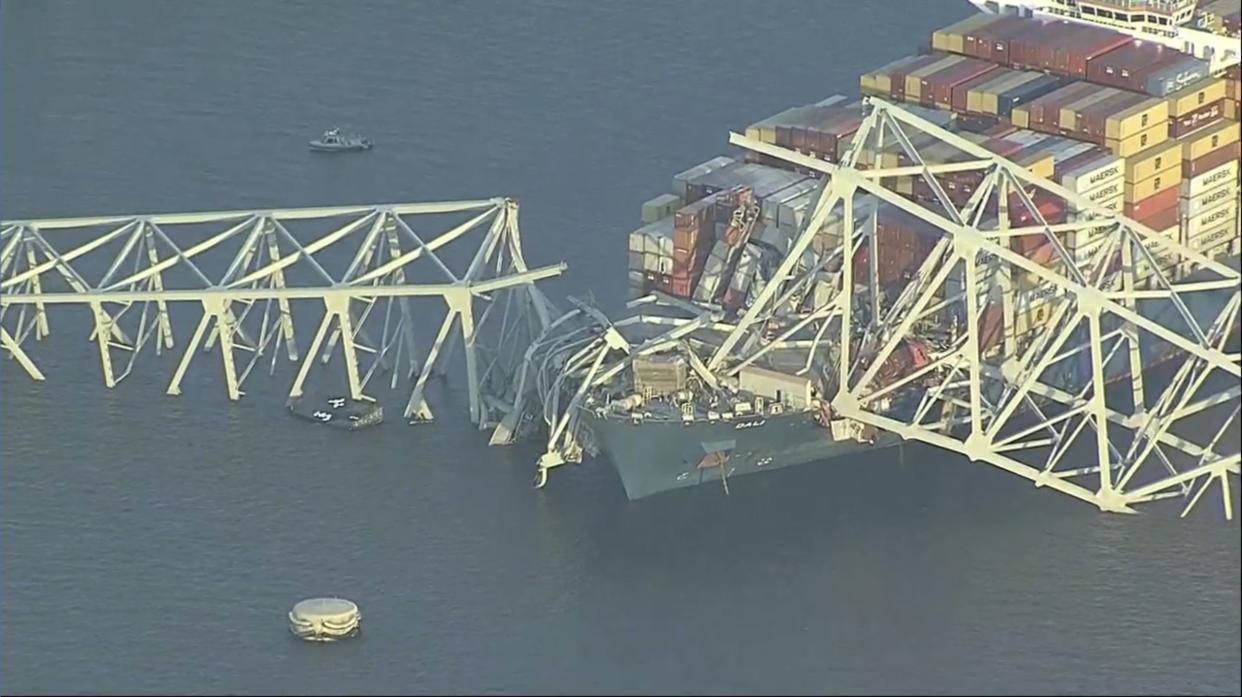 Container ship amid twisted metal sections of destroyed bridge.