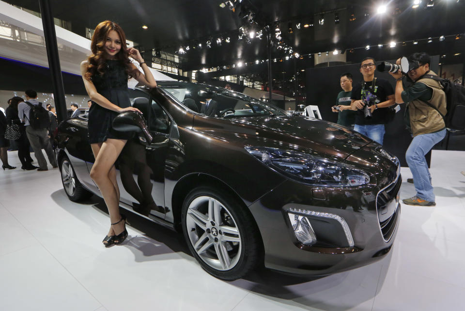 In this Nov. 21, 2013 photo, a model poses with a Peugeot 308CC at the company's booth during the Guangzhou 2013 Auto Show in China's southern city of Guangzhou. French automakers Peugeot and Renault are looking belatedly to China to revive their flagging fortunes but picked a tough time to try to expand. France’s biggest auto brand, PSA Peugeot Citroen, in China since the ‘80s without carving out significant market share, said it will be more aggressive after its local partner, Dongfeng Motor Co., in the week of Feb. 16, 2014 agreed to take a 14 percent stake in PSA. (AP Photo/Kin Cheung)