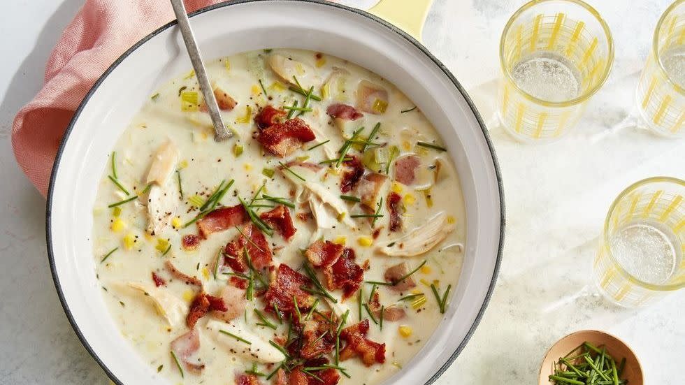 creamy chicken soup with potatoes and bacon in a saucepan and some in a bowl next to it and a bowl of spoons