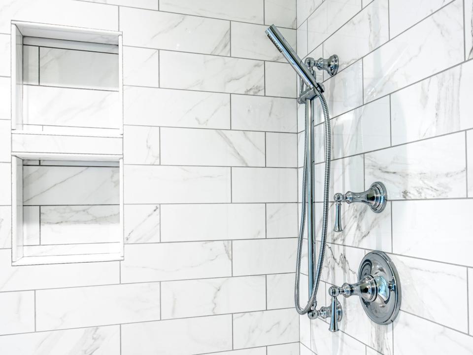 A shower with gray-and-white tiles and a silver shower head with multiple knobs