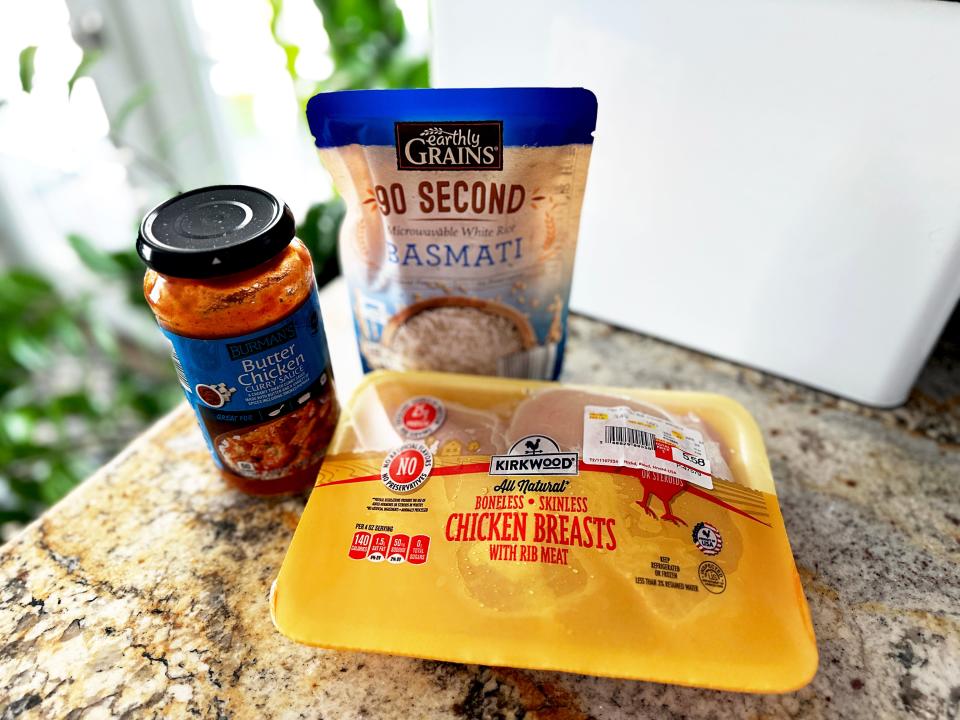 A yellow package of Kirkwood chicken breasts, a blue and tan pouch of Basmati rice, and a jar of butter-chicken curry sauce with a black lid on a stone countertop