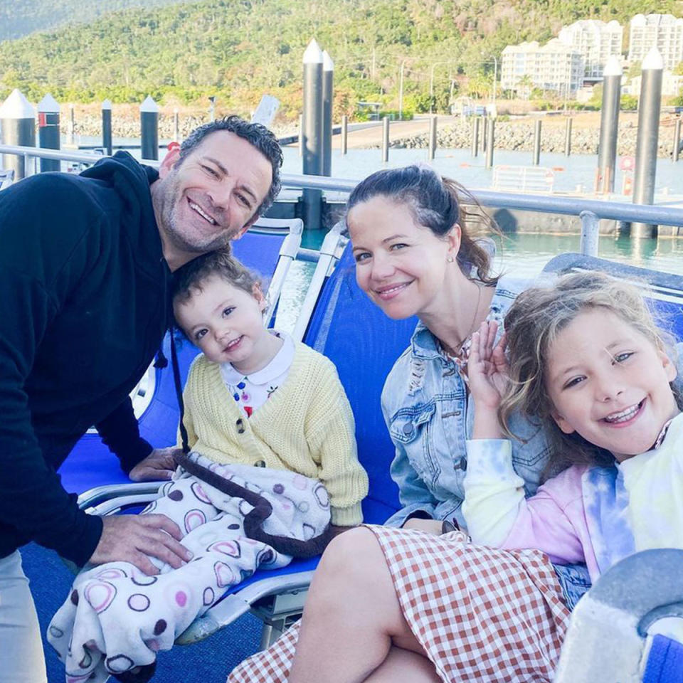 Tammin Sursok, Sean McEwen, Phoenix and Lennon are on a boat. Tammin has her hair tied up and wearing a blue top with a red and white checkered skirt, Sean is in a black hoodie, the two girls are smiling.