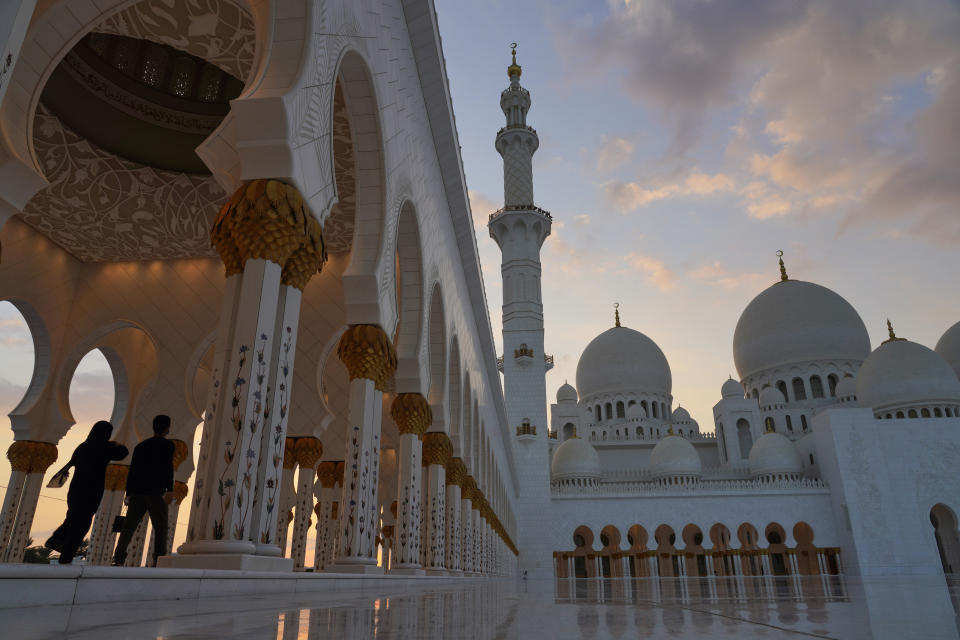 Tourists walk through Sheikh Zayed Grand Mosque at dusk in Abu Dhabi, United Arab Emirates, Wednesday, Dec. 9, 2020. Abu Dhabi announced Wednesday it would resume "all economic, tourism, cultural and entertainment activities in the emirate within two weeks." It attributed the decision to "successes" in halting the spread of the coronavirus. (AP Photo/Jon Gambrell)