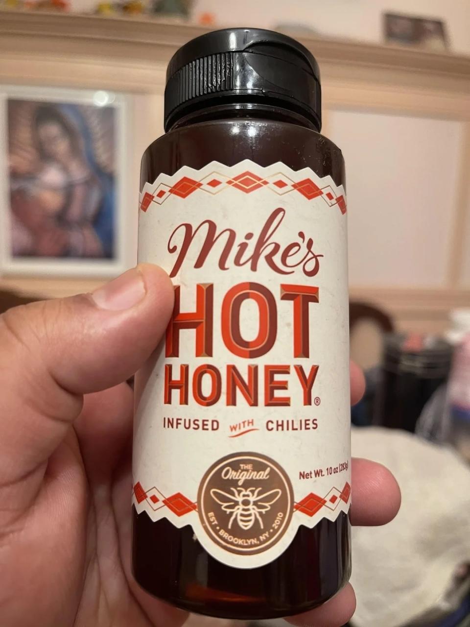 A person holding a bottle of Mike's Hot Honey infused with chilies