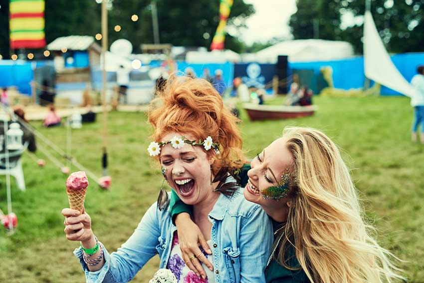 Dos chicas jóvenes disfrutando en un concierto de música entre risas, comiéndose un helado