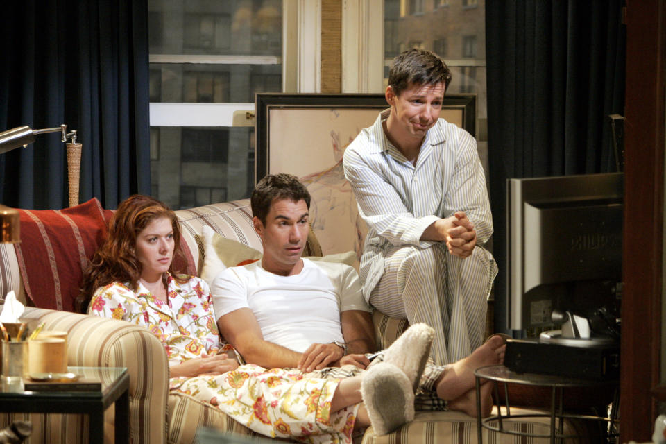 Debra Messing, Eric McCormack, and Sean Hayes sit on a couch in pajamas, appearing engrossed in a show on TV in a cozy room setting