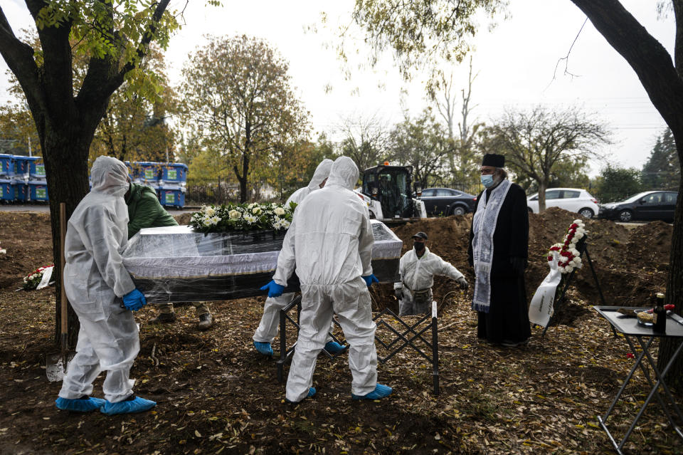 Pallbearers wearing protective suits and gloves, carry a coffin as an Orthodox priest looks on, during a funeral ceremony for a person who died of COVID-19, in the northern city of Thessaloniki, Greece, Saturday, Dec. 5, 2020. Greece is on lockdown until Dec. 7 but government officials say it is too early to say when schools and businesses will reopen due to continued pressure on the state-run health service, with intensive care wards near capacity in parts of the country. (AP Photo/Giannis Papanikos)