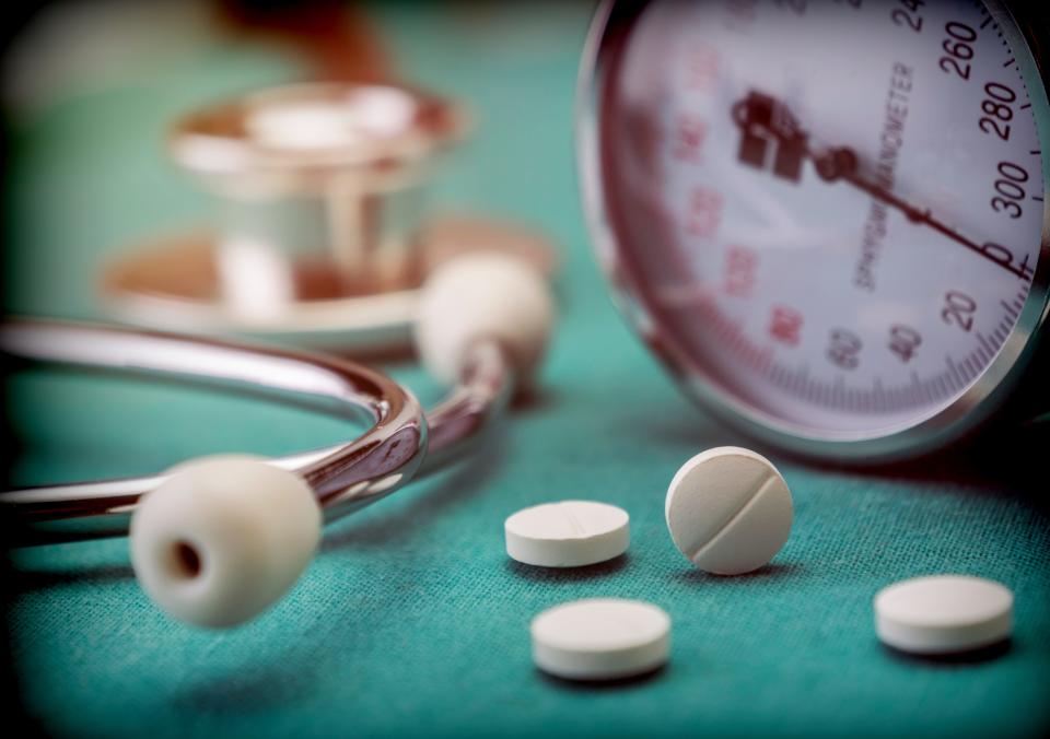 Stock photo showing pills next to a manometer to measure blood pressure and a stethoscope in a hospital, conceptual image.