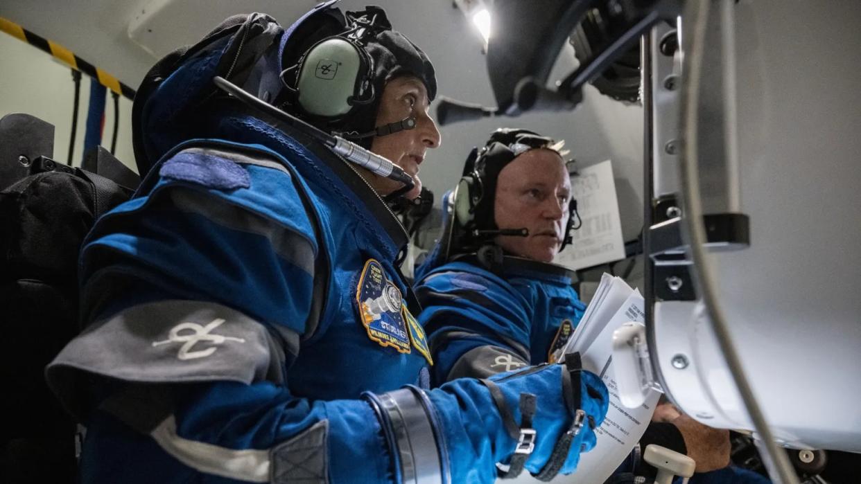  Two astronauts with spacesuits on in a simulator looking at a screen. 