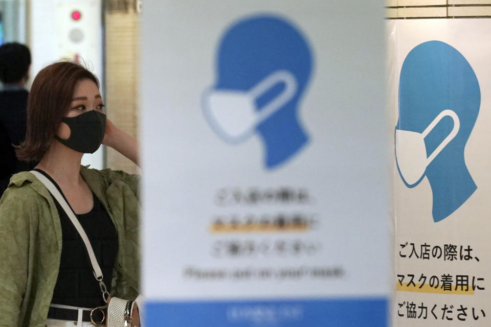 A woman wearing a protective face mask to help curb the spread of the coronavirus walks near signs asking customers to wear protective masks to enter the facility at an underground shopping street in Tokyo Friday, July 3, 2020. Tokyo reported over 100 new cases of the coronavirus on Friday, Governor Yuriko Koike said, amid concerns that recent spikes in the Japanese capital could escalate. (AP Photo/Eugene Hoshiko)