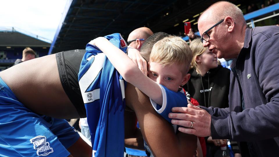 Birmingham's Ethan Laid, with his shirt off, hugs a young fan who is clutching his shirt.