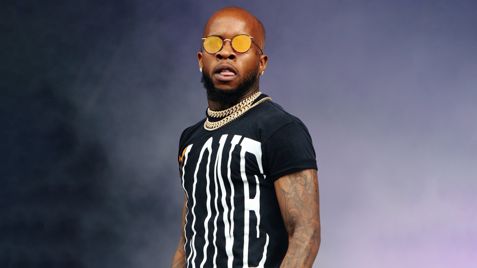 Tory Lanez, wearing sunglasses, looks at the camera.