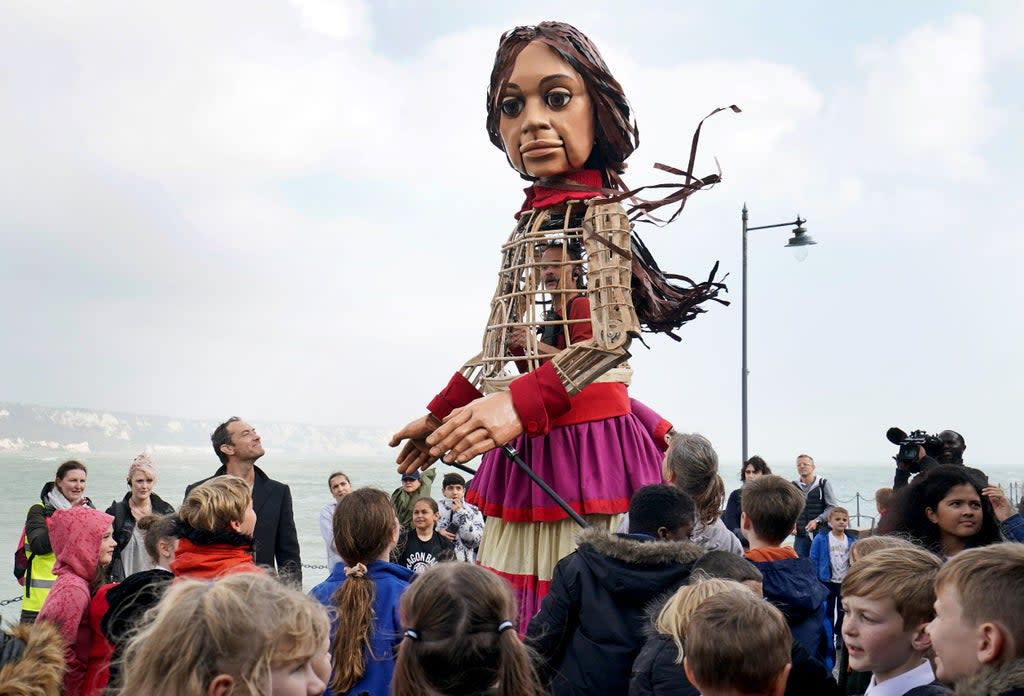 Little Amal, a 3.5-metre-tall puppet of a nine-year-old Syrian girl, is greeted by children from the St Mary’s Primary Academy as she arrives in Folkestone, Kent, as part of the Handspring Puppet Company’s The Walk (Gareth Fuller/PA) (PA Wire)