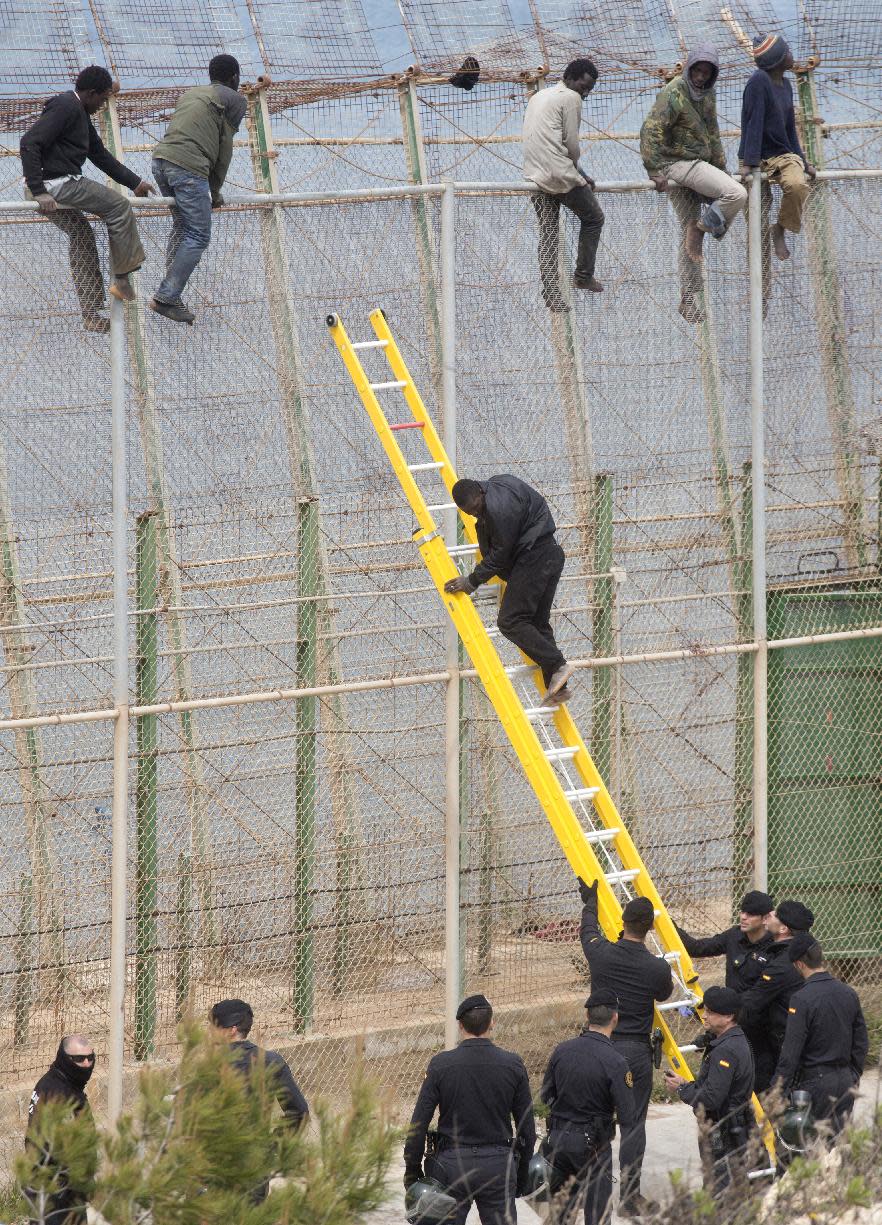 A sub-Saharan migrant climbs dow a ladder held by Spanish Guardia Civil officers as other sit on top of a metallic fence that divides Morocco and the Spanish enclave of Melilla, Thursday, April 3, 2014. Spanish and Moroccan police have thwarted a fresh attempt by dozens of African migrants to try to scale border fences to enter the Spanish enclave of Melilla. Thousands of sub-Saharan migrants seeking a better life in Europe are living illegally in Morocco and regularly try to enter Melilla in the hope of later making it to mainland Spain. (AP Photo/Santi Palacios)