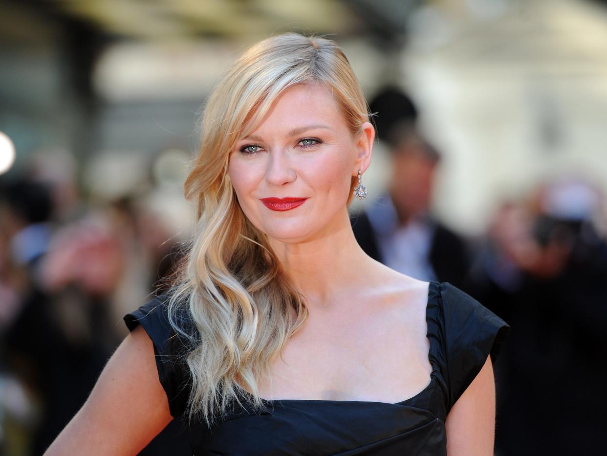 Kirsten Dunst on a red carpet. She wears a black dress.