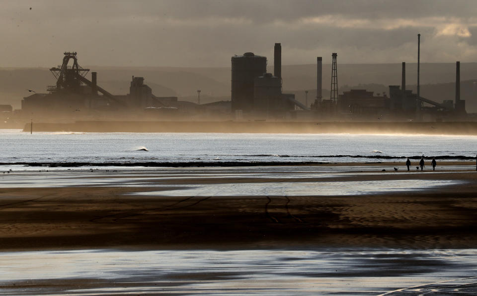 People walk their dogs on the beach in Hartlepool, England, Tuesday, Nov. 12, 2019 with the backdrop of the Redcar steel plant that was shut down in 2015 and will be demolished. Britain's political parties are battling to Hartlepool and place like it: working-class former industrial towns whose voters could hold the key to 10 Downing Street, the prime minister's office.(AP Photo/Frank Augstein)