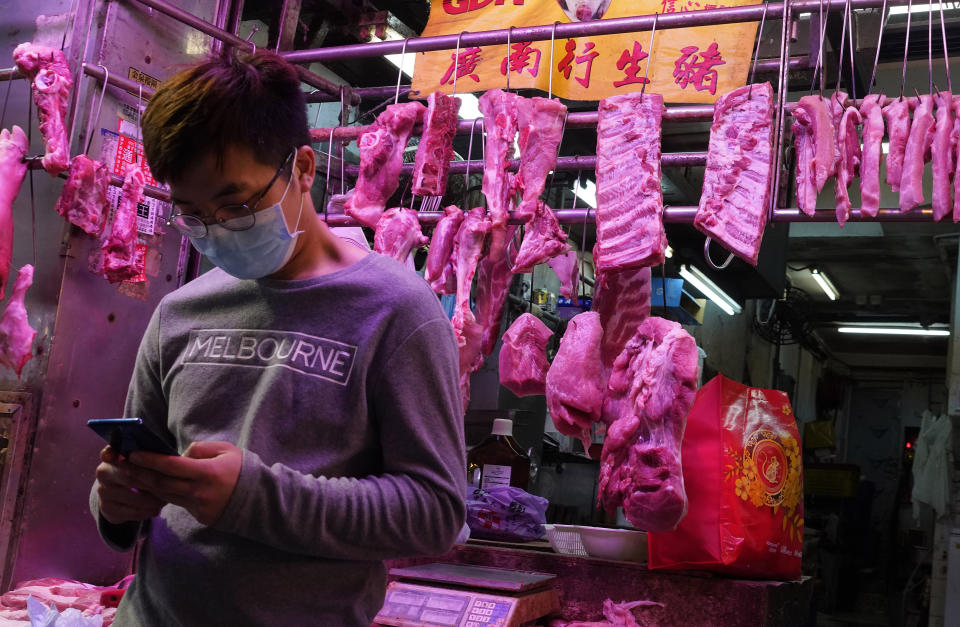 A man wearing face mask looks at his mobile phone in front of a meat booth in Hong Kong, Thursday, Feb. 6, 2020. Ten more people were sickened with a new virus aboard one of two quarantined cruise ships with some 5,400 passengers and crew aboard, health officials in Japan said Thursday, as China reported 73 more deaths and announced that the first group of patients were expected to start taking a new antiviral drug. (AP Photo/Vincent Yu)