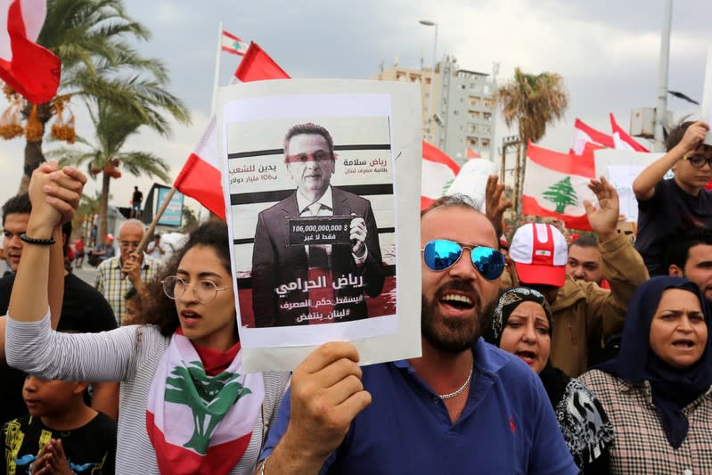 FILE PHOTO: Demonstrators carry Lebanese flags and a banner depicting Lebanon's Central Bank Governor Riad Salameh during an anti-government protest in the southern city of Tyre