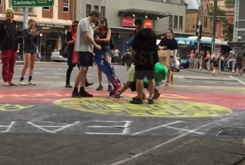 The protesters are seen lighting the flag with what appears to be a lighter. Source: 7 News